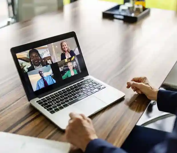 Person at a laptop on a desk, with four people in an online meeting on the screen.