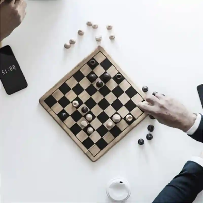 Two people playing chess, with a to-go cup and two phones on the table.