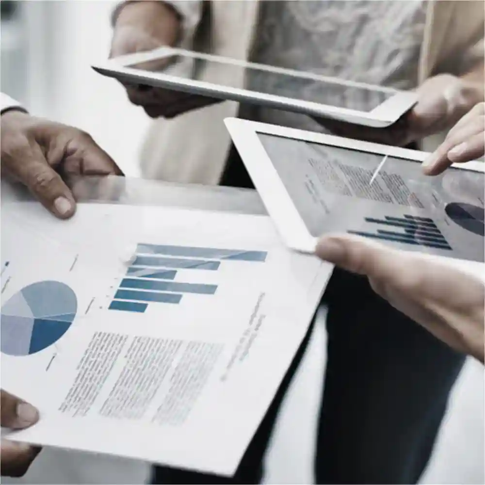 Three people viewing graphs on tablet and paper media.