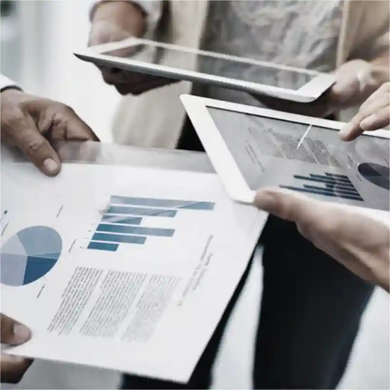 Three people viewing graphs on tablet and paper media.