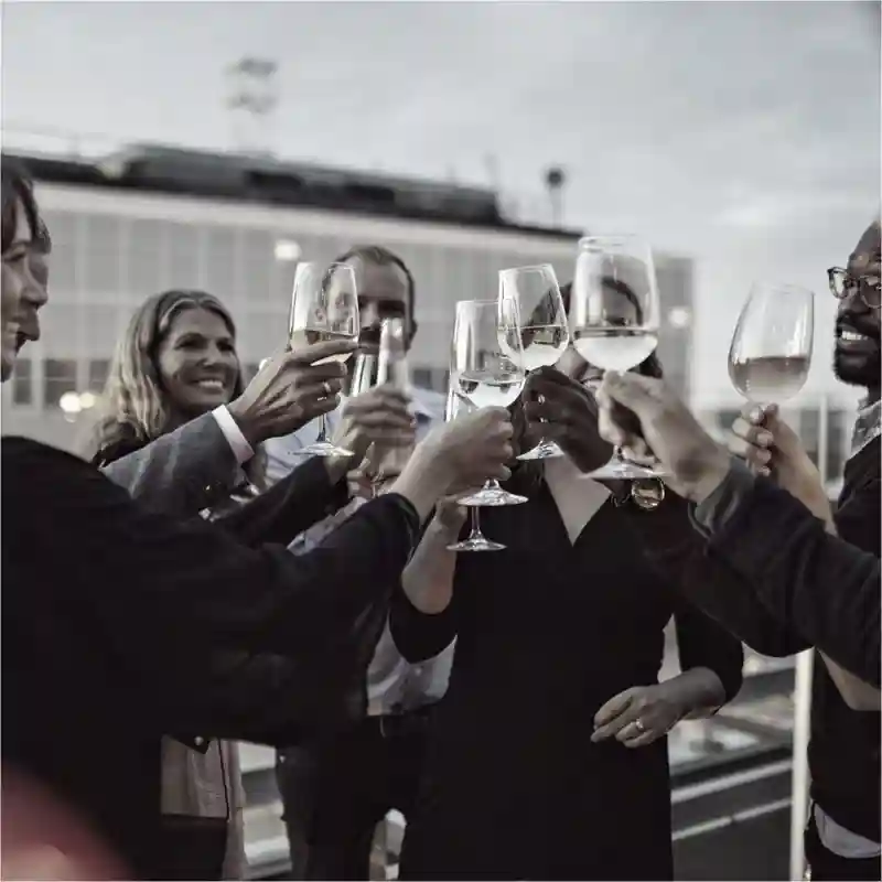 People in formal wear, raising wine glasses, filled with white wine, in celebration.